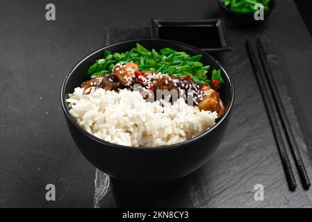 Asiatisches Essen. Asiatisches Kung pao-Huhn mit Reis und grünen Zwiebeln. Kung Pao Hühnchen. Gong Bao Ji Ding auf dunklem Betonhintergrund. Sichuan Kung Stockfoto