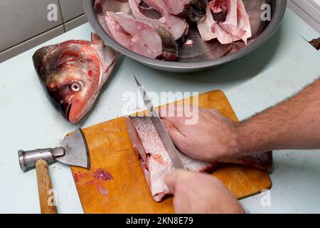 Der Mensch bereitet frischen Silberkarpfen zu. Schneidet es in Steaks mit einem Messer. Hausmannskost-Konzept. Stockfoto