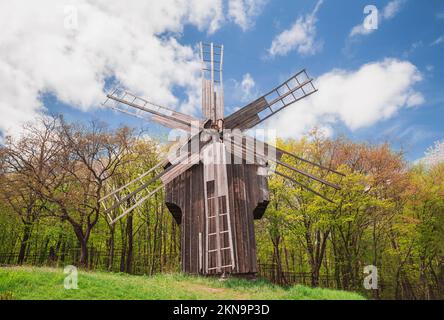 Antike Holzwindmühle auf einem Hügel in der Nähe des Waldes. Ländliche Landschaft Stockfoto