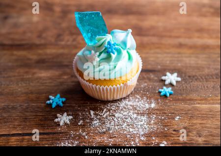 Hausgemachter blauer Cupcake auf einem Holzschreibtisch. Winter- und weihnachtsthema, Schneeflocken auf blauem Eis, frisch und selbstgebacken süß. Stockfoto