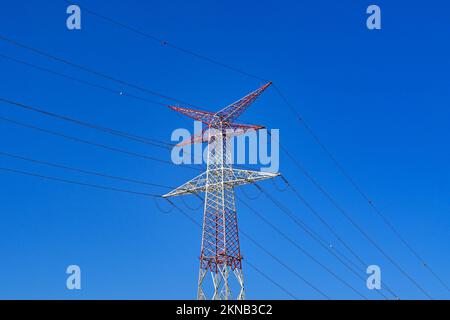 Großer Pylon in einem Stromnetz, isoliert gegen einen tiefen blauen Himmel. Er ist rot und weiß lackiert, um die Sicht auf das Flugzeug zu gewährleisten. Keine Menschen. Stockfoto