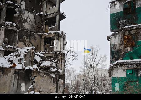 BORODIANKA, UKRAINE - 22. NOVEMBER 2022 - Eine ukrainische Flagge fliegt auf dem Pol nahe den Ruinen eines Wohnungsgebäudes, das von russischen Truppen zerstört wurde Stockfoto