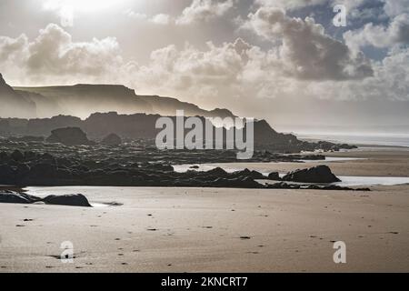 Dramatisches Novemberwetter in der Sandymouth Bay in Cornwall mit sonniger Hintergrundbeleuchtung und Dunst Stockfoto