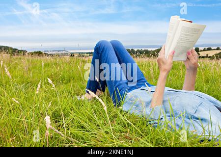 Frau, die auf einem grasbewachsenen Feld liegt und liest Stockfoto