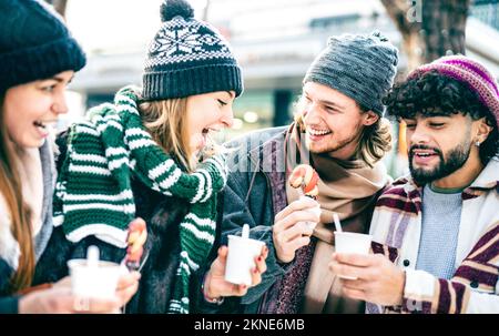 Fröhliche Freunde, die im Winter auf dem Weihnachtsmarkt Süßigkeiten essen - Vintage-Urlaubskonzept mit jungen Leuten, die zusammen abhängen Stockfoto