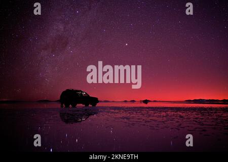 Nachthimmel in den Uyuni Salzebenen, Bolivien, mit einem Geländewagenparkplatz auf der Oberfläche. Stockfoto