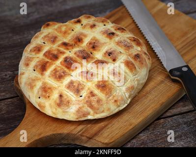 türkisches Fladenbrot mit schwarzem Kreuzkümmel auf Holzbrett mit Brotmesser, rundes Weizenbrot für Döner Kebab Stockfoto