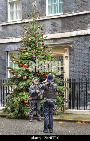 London, Großbritannien. 27.. November 2022. Zwei Polizisten machen Fotos mit dem Weihnachtsbaum. Der Downing Street Christmas Tree ist mit bunten Baumbällen dekoriert und verleiht der ansonsten grauen Straße trotz des schlechten Wetters einen festlichen Touch. Kredit: Imageplotter/Alamy Live News Stockfoto