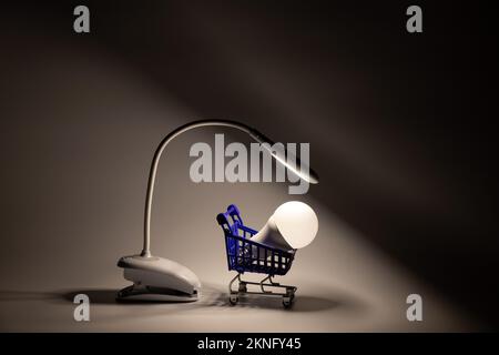 Flexible Desktop-LED-Lampe auf der Batterie und LED-Glühbirne in einem Supermarktkorb im Dunkeln auf dem Tisch glänzt, Licht und Technologie und Geschäft Stockfoto