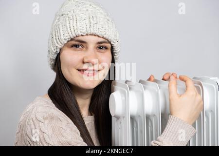 Eine brünette Frau mit Hut umarmt einen Ölwärmer und wärmt sich im Winter auf. Stockfoto