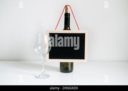 Eine Flasche Wein, ein Glas und ein leeres Schildmodell. Flasche Wein mit leerem Glas und Tafelmockup auf dem Tisch. Stockfoto