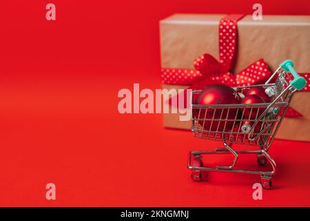 Weihnachtsangebot Webbanner mit Mini-Wagen mit Geschenkbox und roten Weihnachtsbällen auf rotem Hintergrund. Minimale Weihnachtseinkäufe Stockfoto