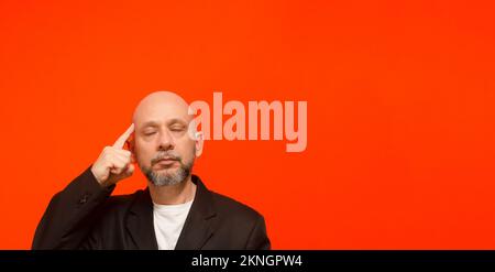 Geschäftsmann, trägt eine schwarze Anzugjacke, schlau und aufmerksam. Isoliert auf orangefarbenem Hintergrund. Stockfoto