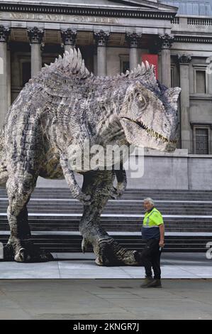 Ein Arbeiter, der vor Einem großen Bildschirm mit einem projizierten Bild Eines T-Rex vor der National Gallery, London UK, läuft Stockfoto