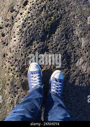 Die Sichtweise einer Person, die auf ihre Schuhe schaut, während sie auf einem Felsen steht Stockfoto