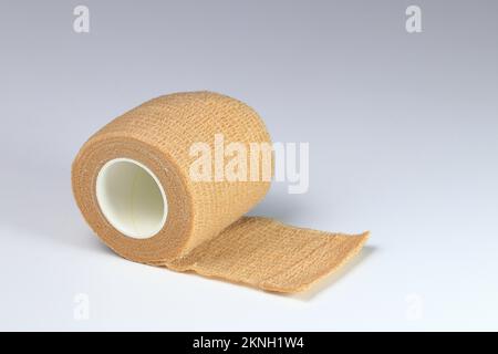 Brauner elastischer Bindeverband, medizinischer bindender elastischer Verband oder elastischer Bandage aufgerollt auf weißem Hintergrund. Stockfoto