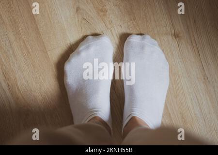 Weiße Socken auf dem Boden. Damenschuhe. Warmes Bekleidungskonzept. Bequeme Baumwollkleidung. Familiäre Hintergründe. Weiße Socken auf Mädchenfüßen. Stockfoto