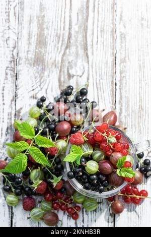 Im Sommer frische Stachelbeeren mit roter und schwarzer Johannisbeere in Glasbecher auf Holztisch Stockfoto