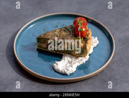 Runde TORTE mit Spinat und Fisch. Herzhafte Quiche mit Lachs und Spinat, Nahaufnahme auf dem Teller. Stockfoto