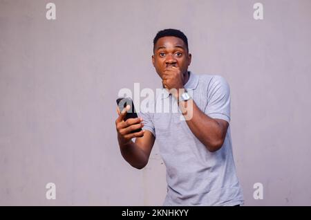 Ein fröhlicher afroamerikanischer Mann überraschte, was er auf seinem Handy auf grauem Hintergrund sah Stockfoto