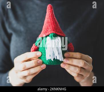 Lustiges Strickspielzeug in Frauenhänden. Mädchen mit handgemachtem Weihnachtsgeschenk. Süßer Zwerg mit weißem Bart. Winterdekoration. Weihnachtsmann-Spielzeug in den Händen von Mädchen. Stockfoto