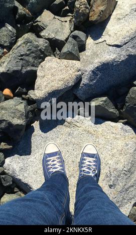 Die Sichtweise einer Person, die auf ihre Schuhe schaut, während sie auf einem Felsen steht Stockfoto