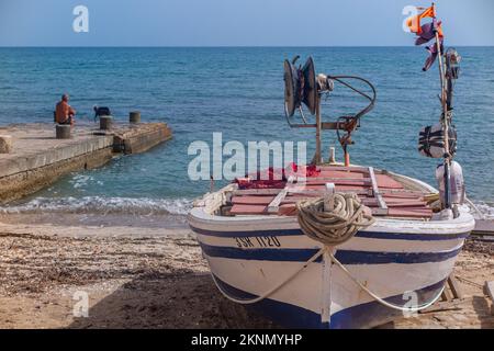 Ein Mann und ein Hund auf einem Steg mit einem Fischerboot fuhren an Land in einem traditionellen sizilianischen Fischerdorf Stockfoto