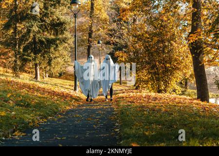 Ein lustiges Bild von zwei wandelnden Menschen in Geisterkostümen und Sonnenbrillen Stockfoto