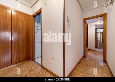 Korridor eines Hauses mit Parkettschachbrettboden, Zugang zu anderen Zimmern und ein eingebauter Kleiderschrank mit hässlichen Holztüren Stockfoto