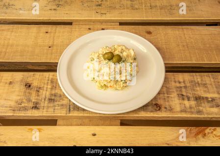 Teller mit Ensaladilla rusa, typisch zum Servieren in einer Tapas-Bar auf einer Oberfläche von unlackierten Holzplanken Stockfoto