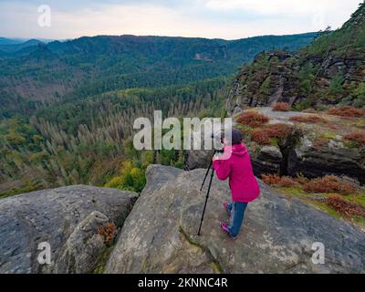 Eine Fotografin macht Fotos mit der Kamera in den Morgenhügeln. Naturfotograf mit Fotoausrüstung auf Felsen Stockfoto