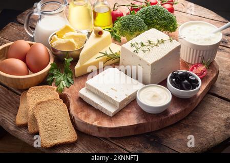 Frische Milchprodukte, isoliert auf Holzhintergrund. Collage aus Milch, Käse, Butter, Ei, Gemüse, Kräuter, Brot. Stockfoto