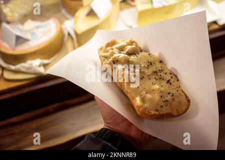 Handgriff Raclette, geschmolzener Käse im Schweizer Stil, auf Brot gekratzt, vor dem Käsesaal auf dem Weihnachtsmarkt. Stockfoto