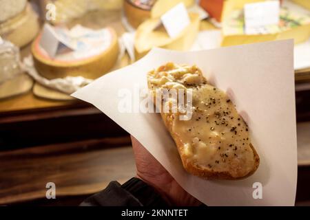 Handgriff Raclette, geschmolzener Käse im Schweizer Stil, auf Brot gekratzt, vor dem Käsesaal auf dem Weihnachtsmarkt. Stockfoto