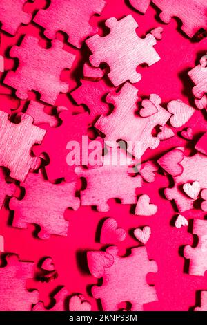 Pinke Kunstwerke auf verstreuten Puzzleteilen zwischen zufälliger Herzform. Spiel der Romantik Stockfoto