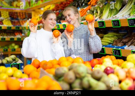 Glückliches Teenager-Mädchen mit Mutter hält reifen Orangen in greengrocery speichern Stockfoto