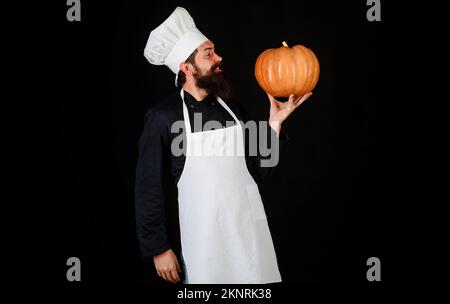 Bärtiger Koch in weißer Schürze und Hut mit Kürbis. Herbstessen. Gesundes Bio-Gemüse Stockfoto