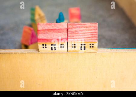 TwoCottages mit rotem Dach auf grauem Boden. Kleine Spielzeughäuser aus Holz an der Grenze. Kinderspiel. Ein Modeldorf. Bau- und Architekturkonzept Stockfoto