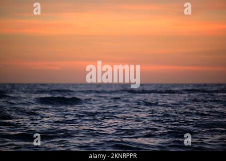 Dramatische rote Meereswellen bei Sonnenuntergang mit weichem, dunklem Meerwasser am Abend Stockfoto