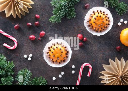 Dunkler Winterhintergrund mit duftenden Pomanderbällen. Klassische Dekoration - Mandarine mit Nelken. Handgefertigte Papiersterne aus braunem Backpapier Stockfoto