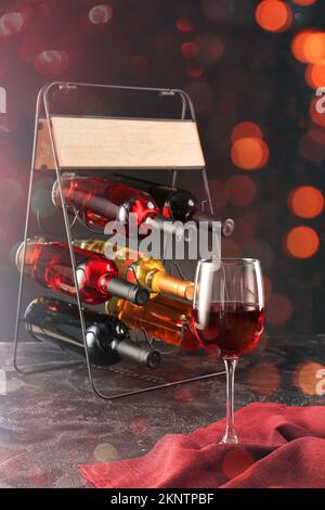 Halter mit Flaschen und Glas Wein auf dunklem Hintergrund Stockfoto