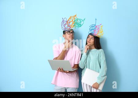 Aufmerksames junges Paar mit vielen Pfeilen im Kopf und mit Laptops auf blauem Hintergrund Stockfoto