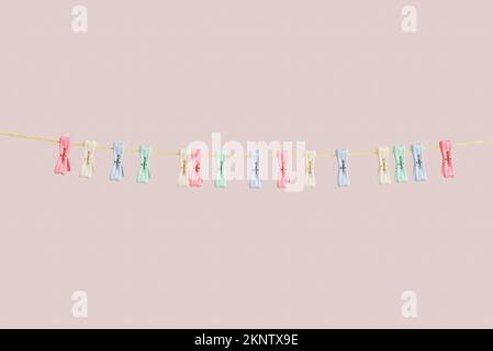 Verschiedene Plastikkleiderinnen hängen am Seil vor farbigem Hintergrund Stockfoto
