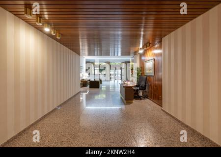 Portal eines Wohnhauses mit Treppen und Granitböden, papierverzierten Wänden und einem Aufzug mit brauner Metalltür und einer Lounge für Besucher und einem de Stockfoto