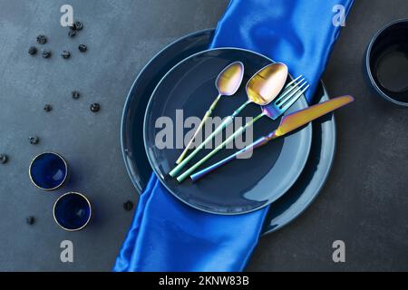 Verschiedene blaue porzellanteller mit blauer Tischdecke, goldfarbenen blauen Gläsern, Blaubeeren und schillerndem Besteck Stockfoto