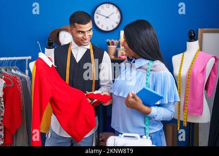 Mann und Frau Schneiderinnen halten Touchpad und T-Shirt im Nähstudio Stockfoto