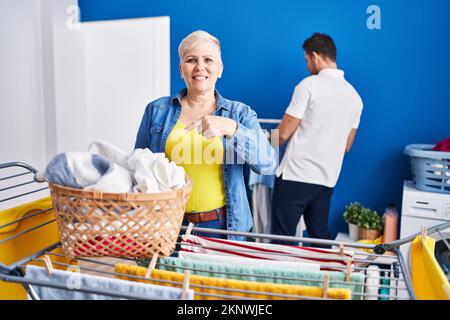 Hispanische Mutter und Sohn hängen Kleider an der Wäscheleine auf und lächeln fröhlich mit Hand und Finger Stockfoto
