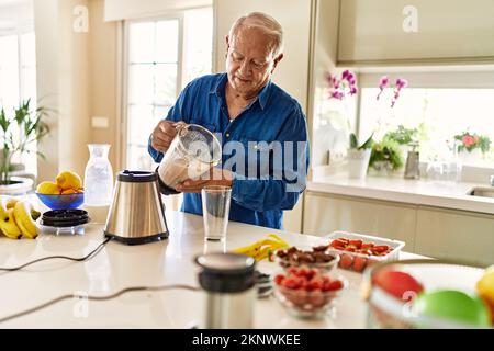 Älterer Mann, der in der Küche Smoothie auf Glas gießt Stockfoto