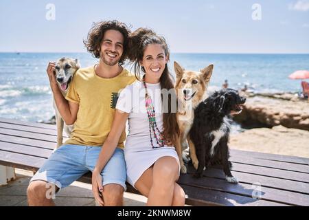 Mann und Frau Paar lächeln selbstbewusst und umarmen sich am Meer mit Hunden Stockfoto