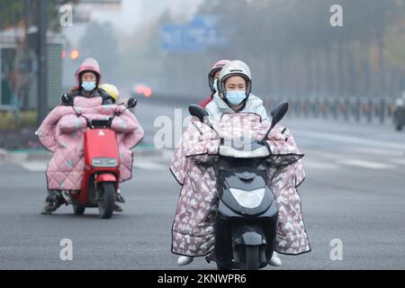 LIANYUNGANG, CHINA - 28. NOVEMBER 2022 - Menschen tragen dicke Winterkleidung und fahren Fahrräder auf einer Straße in Lianyungang, dem östchinesischen Jiangsu Prov Stockfoto